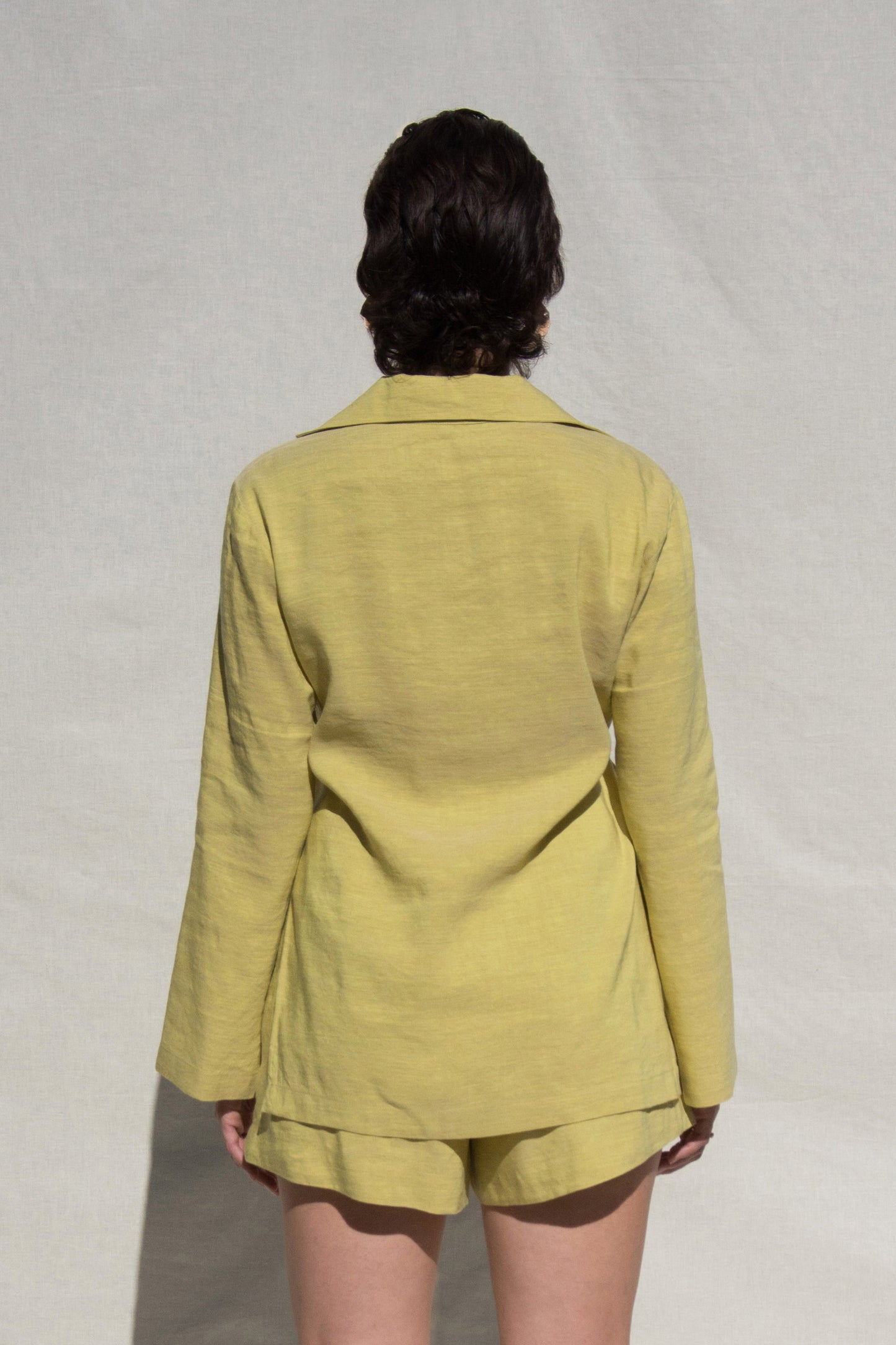 Back shot of model wearing long sleeve shirt and short set in Green Linen. Wearing Ceramic Pink earrings